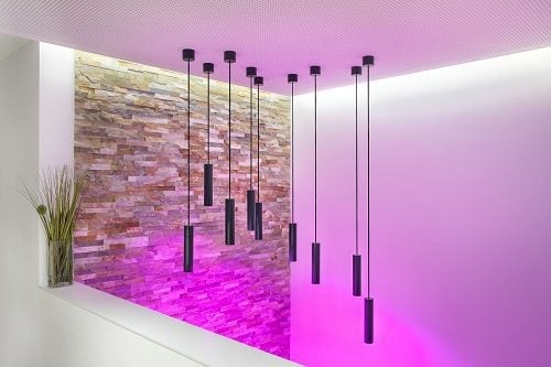 Modern interior with geometric LED pendant lights suspended above glowing magenta floor and exposed brick wall accents
